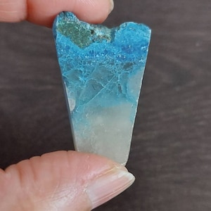 Op de afbeelding: Een blauwe en witte kristal met een puntige punt. De kristal heeft een gelaagde uitstraling met een donkerblauwe laag aan de bovenkant en een lichtblauwe laag aan de onderkant.