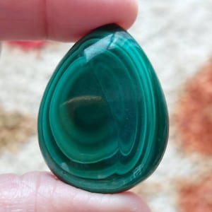 Op de afbeelding: Een groene malachiet cabochon met een traanvorm en concentrische kleurringen.
