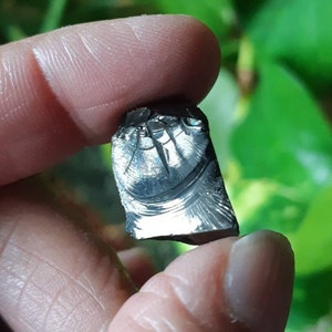 K&ouml;nnte beinhalten: Nahaufnahme eines unregelm&auml;&szlig;ig geformten, dunkelgrauen, metallischen Steins mit einem silbrigen, irisierenden Schimmer. Der Stein hat eine einzigartige, strukturierte Oberfl&auml;che mit einem Muster aus Linien und Wirbeln.