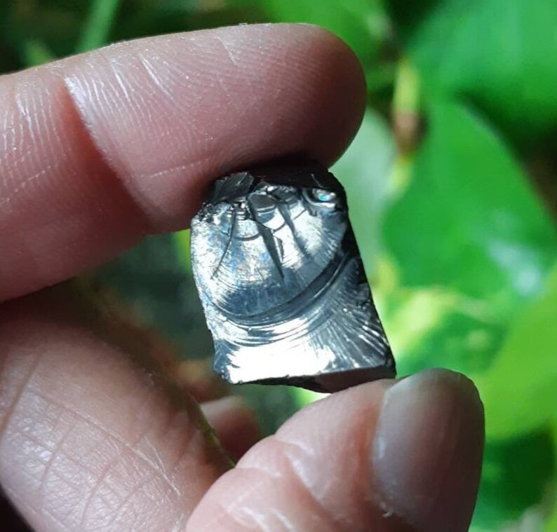 K&ouml;nnte beinhalten: Nahaufnahme eines unregelm&auml;&szlig;ig geformten, dunkelgrauen, metallischen Steins mit einem silbrigen, irisierenden Schimmer. Der Stein hat eine einzigartige, strukturierte Oberfl&auml;che mit einem Muster aus Linien und Wirbeln.