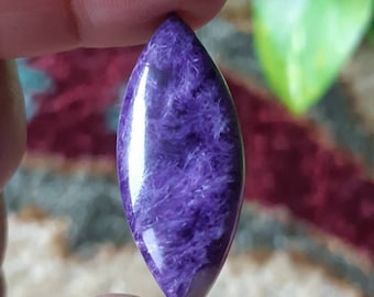 Könnte beinhalten: Ein violetter und weißer Cabochon-Edelstein in Birnenform mit glänzender, polierter Oberfläche.