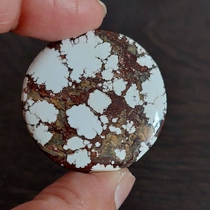 Könnte beinhalten: Ein runder, weißer und brauner Cabochon-Edelstein mit einem marmorierten Muster.