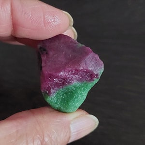 May include: A rough, natural ruby and green gemstone with a pink and green colour gradient. The gemstone is a rough, unpolished, natural stone.