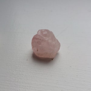 Può includere: Un piccolo cristallo di quarzo rosa grezzo di colore rosa chiaro.