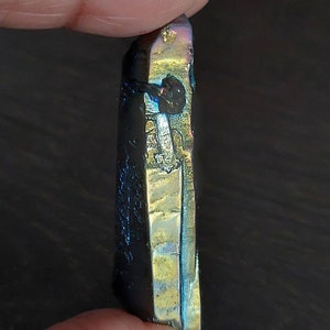 May include: A black iridescent crystal point with a gold sheen. The crystal is pointed at the top and has a flat base.
