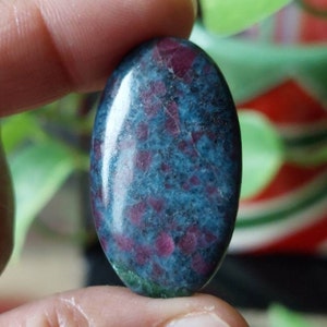 Peut inclure: Pierre précieuse ovale en cabochon avec une base bleue et des inclusions rouges. La pierre a une surface lisse et polie.