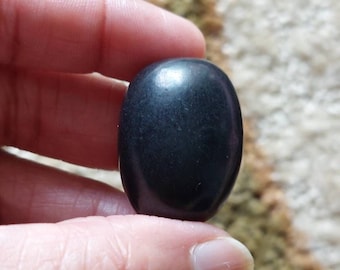 May include: A smooth, black oval-shaped stone. The stone is polished and has a glossy finish.