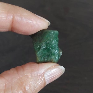 May include: A rough, green emerald gemstone with a natural, unpolished finish.