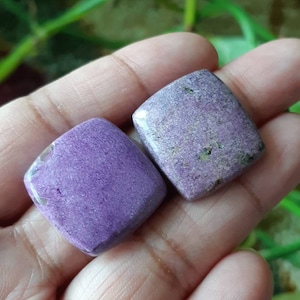 以下が含まれることがあります： 2つの正方形の紫と白の宝石のカボション。カボションは粗くて質感のある表面をしています。