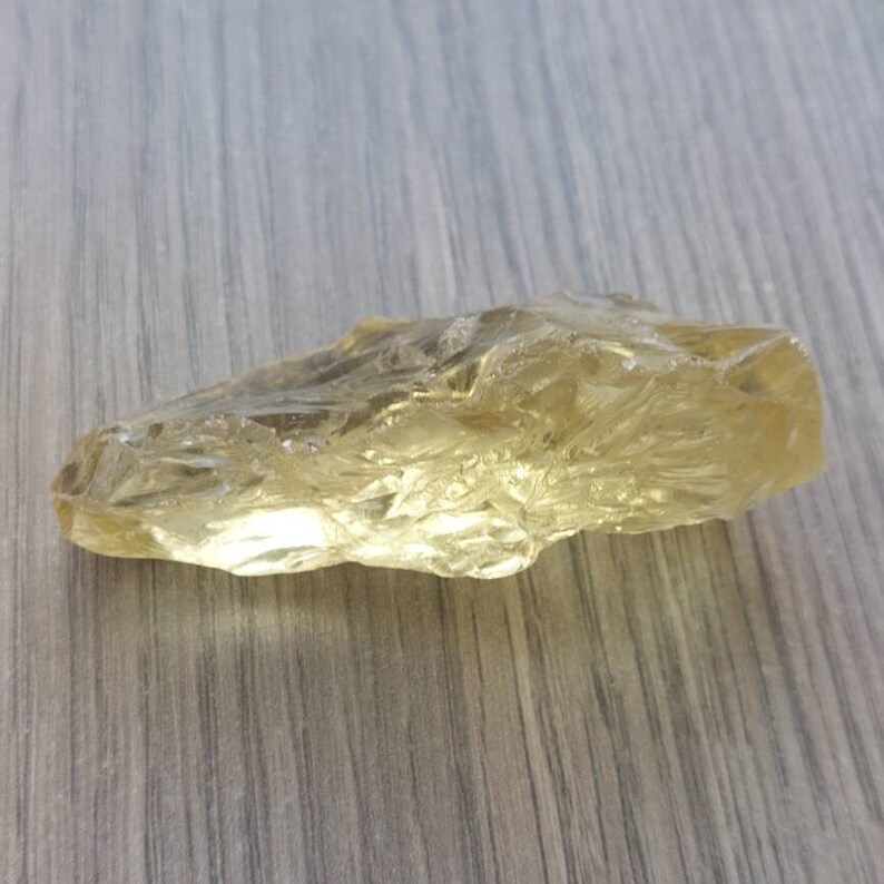 K&ouml;nnte beinhalten: Ein gro&szlig;er, klarer, gelber Kristall mit einer rauen, nat&uuml;rlichen Textur. Der Kristall ist durchscheinend und hat einen leichten goldenen Farbton.