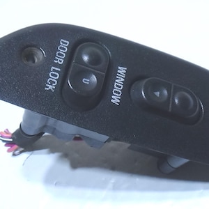 Puede incluir: Panel de control de puerta de coche negro con botones para el cierre de puertas y los controles de ventanas. El panel tiene las palabras "DOOR LOCK" y "WINDOW" impresas.