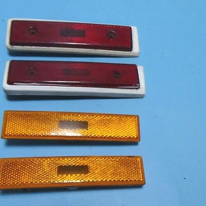 May include: Four rectangular car reflectors, two red and two amber. The red reflectors have a white backing and the amber reflectors have a yellow backing.