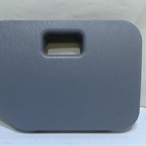 Peut inclure: Un panneau en plastique gris rectangulaire avec une surface texturée et une découpe de poignée rectangulaire. Le panneau a des coins arrondis et un bord légèrement incurvé d'un côté. Le fond est une surface blanche unie.