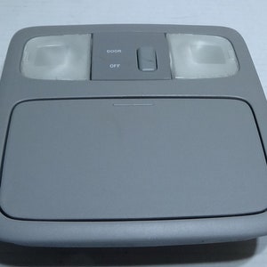 May include: Gray car interior dome light with a built-in compartment and a switch labeled "DOOR" and "OFF".