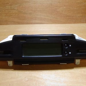 Puede incluir: Un componente negro del salpicadero de un coche con una pantalla de visualización rectangular y dos botones etiquetados como 'N' y 'M'. El componente tiene una parte superior blanca y está montado sobre una superficie clara. La palabra 'PASSENGER' es visible.