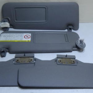 May include: Several gray car sun visors are displayed. Two visors are fully assembled, and one is partially disassembled. The visors have a rectangular shape with a recessed area. The image shows the front and back of the visors.
