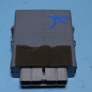 Op de afbeelding: Een grijs elektronisch module met een zwart schuimkussen en een connector met vier pinnen. Het module heeft tekst erop die luidt "89431-12010 181640 717531 TOYOTA 12V MADE IN JAPAN".