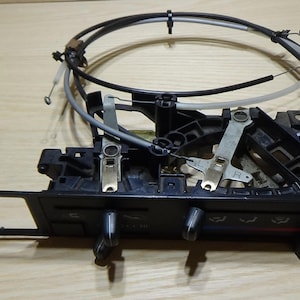 May include: A black car air conditioning control panel with knobs and levers. The panel has a rectangular opening and is connected to various wires and cables. The image is taken from a top-down perspective.