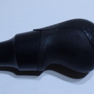 Op de afbeelding: Zwarte versnellingspookknop met een getextureerd oppervlak en een afgeronde vorm.