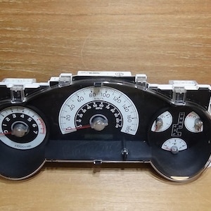 May include: A black and white car dashboard instrument cluster with a speedometer, tachometer, and fuel gauges. The speedometer reads up to 180 km/h. The gauges are set against a black background.