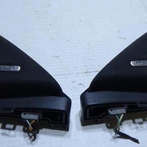 May include: Two black car interior trim pieces. Each piece has a triangular shape with a curved top and a rectangular base. The text "mach audio system" is visible on a silver plate on each piece. Wires extend from the base.