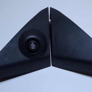 May include: Two black, triangular automotive interior trim pieces. One piece has a circular button with a small, white graphic. The other piece is a solid triangle. The pieces are set against a white background.