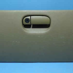Può includere: Uno sportello beige per vano portaoggetti di un'auto con una chiusura nera e una maniglia beige.