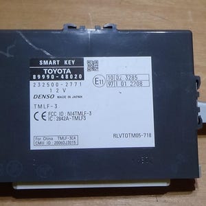 May include: A black Toyota Smart Key module with a white label. The label displays the Toyota logo, model number, and technical details. The module has metal brackets and is marked "DENSO MADE IN JAPAN".