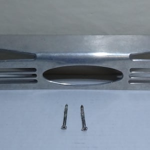 Könnte beinhalten: Eine silberne Wandhalterung aus Metall mit zwei Schlitzen und einer ovalen Öffnung. Sie wird mit zwei silbernen Schrauben geliefert.