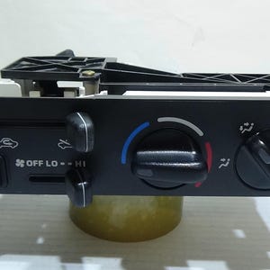 May include: Black plastic car air conditioning control panel with buttons for A/C, fan speed, temperature, and recirculation. The panel has the text "OFF LO - HI" and "USE WITH" printed on it.