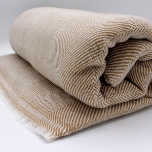 May include: A brown and white herringbone patterned throw blanket with a fringed edge. The blanket is rolled up and the fringe is visible.