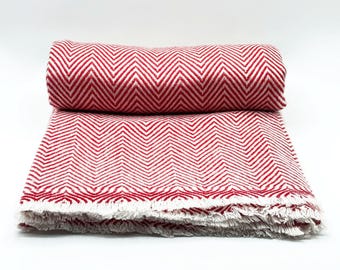 May include: A folded red and white herringbone patterned blanket. The blanket is made of a soft material and has a fringed edge. The blanket is rolled up at the top and folded at the bottom.
