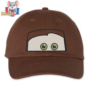 May include: Brown baseball cap with an embroidered cartoon face with green eyes.