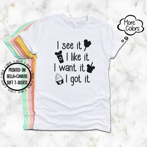 May include: White Bella+Canvas soft t-shirt with the text "I see it, I like it, I want it, I got it" in black. The design includes Mickey Mouse-themed icons. The shirt also has a "More Colors" graphic.