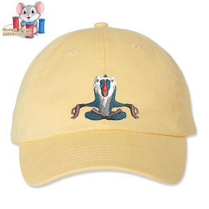 May include: A yellow baseball cap with an embroidered image of a mandrill meditating. The mandrill is blue, white, and red.