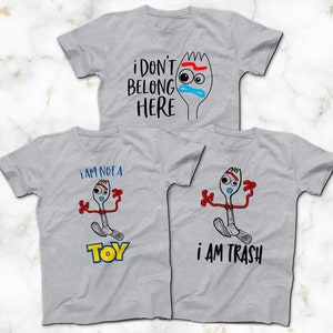 May include: Three gray t-shirts with a cartoon image of a fork with a face and the text "i don't belong here", "i am not a toy", and "i am trash".