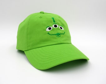 May include: A bright green baseball cap with an embroidered alien face. The alien has three eyes and a small mouth.