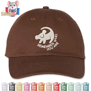 May include: A brown baseball cap with a curved brim. The cap features a white embroidered design of a mouse and the words "REMEMBER YOU ARE". The cap has a six-panel design with a top button and an adjustable strap.