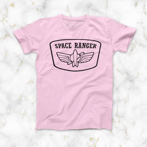 May include: Pink t-shirt featuring a black graphic of a space ranger patch with the text "SPACE RANGER" and a rocket ship with wings.