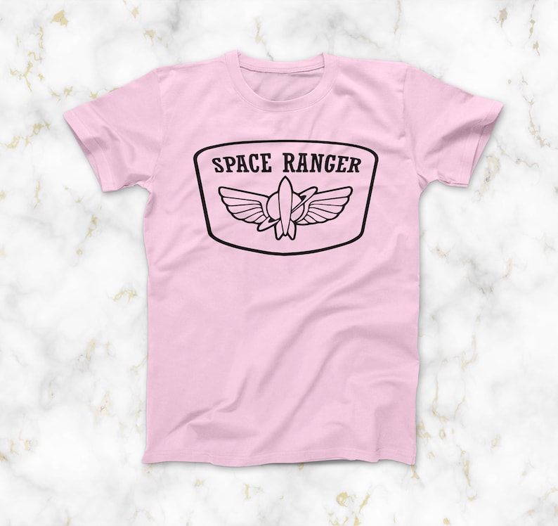 May include: Pink t-shirt featuring a black graphic of a space ranger patch with the text "SPACE RANGER" and a rocket ship with wings.