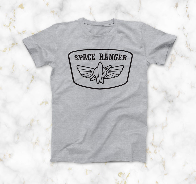May include: A grey t-shirt with a black graphic of a space ranger patch. The patch features a rocket ship with wings and the text "SPACE RANGER".