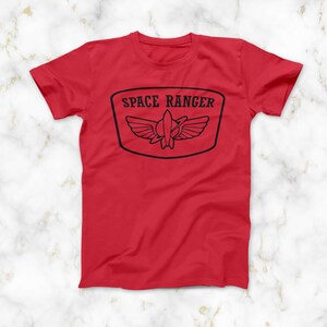 May include: Red t-shirt with a black graphic of a space ranger badge with the text "SPACE RANGER" on it.