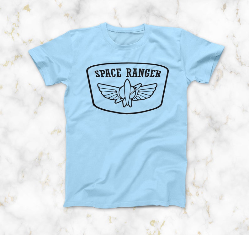 May include: A light blue t-shirt with a black graphic of a space ranger patch. The patch features a rocket ship with wings and the text "SPACE RANGER".