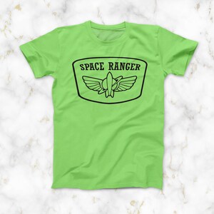 May include: A lime green t-shirt featuring a black graphic of a space ranger badge. The badge depicts a rocket ship with wings and the text "SPACE RANGER".