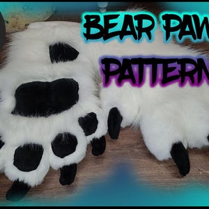 May include: A pair of white furry bear paw hand puppets with black paw pads. The puppets are on a brown surface. The text "BEAR PAWS PATTERN" is in the background. A PDF icon is in the lower right corner.