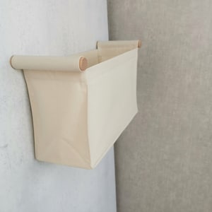 Peut inclure: Un bac de rangement mural en toile beige avec des poignées en bois. Le bac est vide et a une forme rectangulaire.