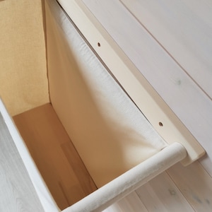 May include: A white canvas storage bin with a wooden frame and a fabric handle. The bin is mounted to a white wooden wall.