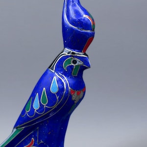 May include: A blue ceramic figurine of the Egyptian god Horus, depicted as a falcon with a human head. The figurine is decorated with intricate details and colorful accents.