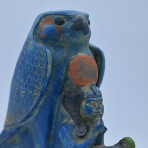 May include: A blue and orange ceramic statue of the Egyptian god Horus, depicted as a falcon with a human head. The statue is detailed with intricate carvings and paint.