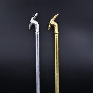 Puede incluir: Dos brochetas decorativas de metal. Una es plateada y la otra dorada. Cada una presenta una cabeza de animal estilizada en la parte superior y un diseño en forma de tenedor en la parte inferior. Las brochetas se muestran sobre un fondo oscuro. Miden unos 25 cm de largo.